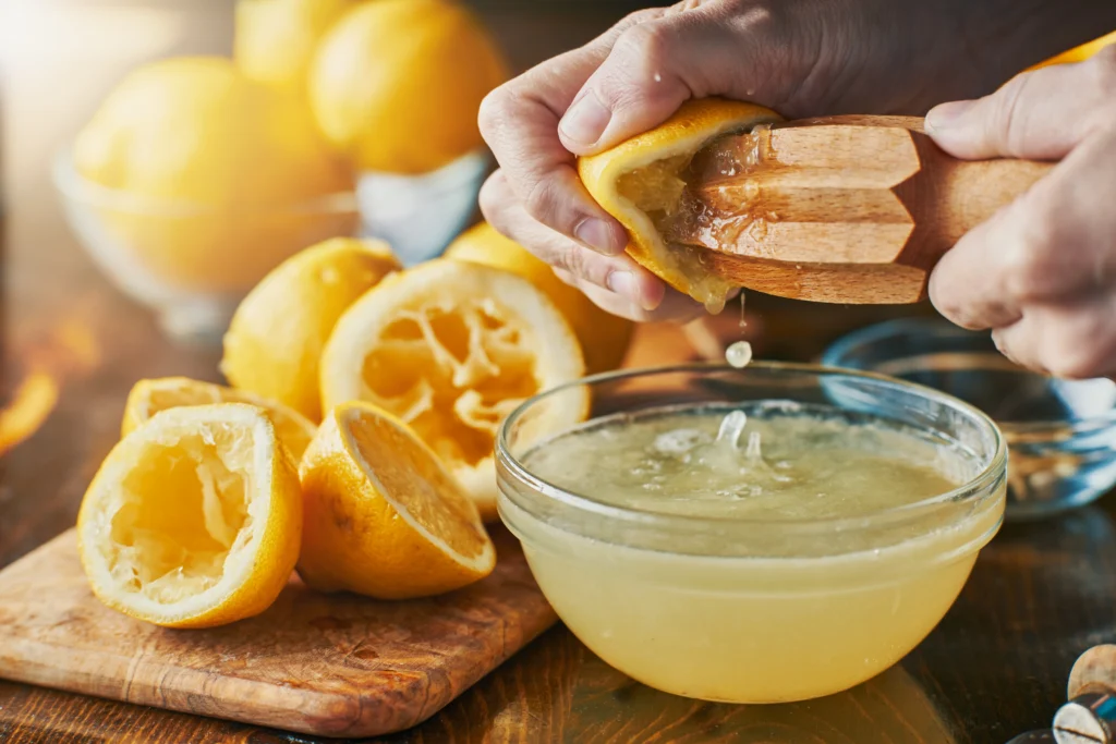 Fresh lemons being juiced with a wooden reamer into a glass bowl