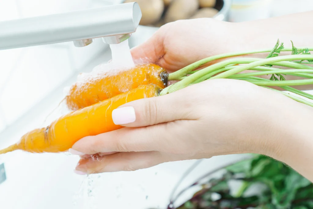 A person scrubbing carrots under running water in a kitchen sink