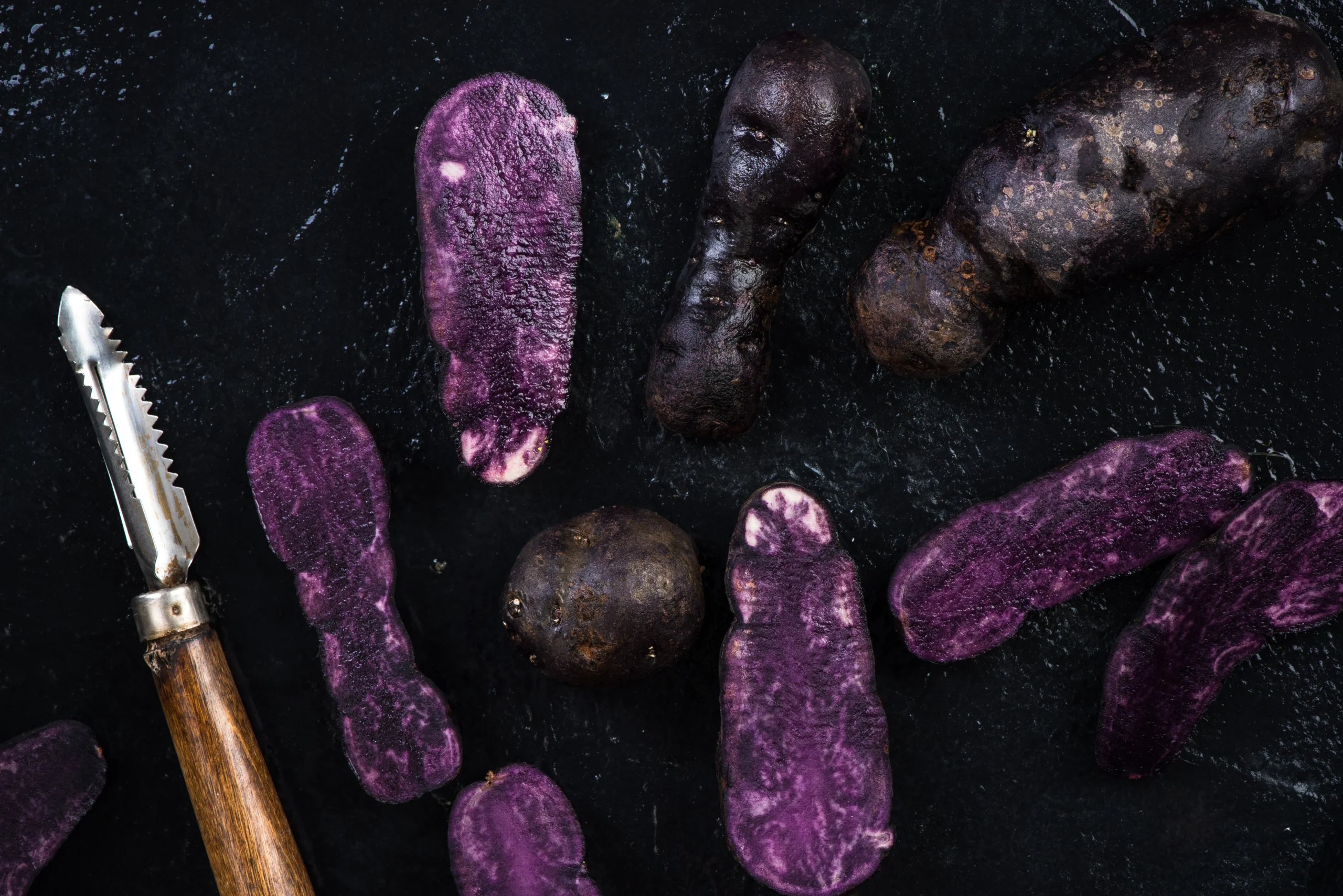 Fresh purple sweet potatoes sliced and whole on a dark surface